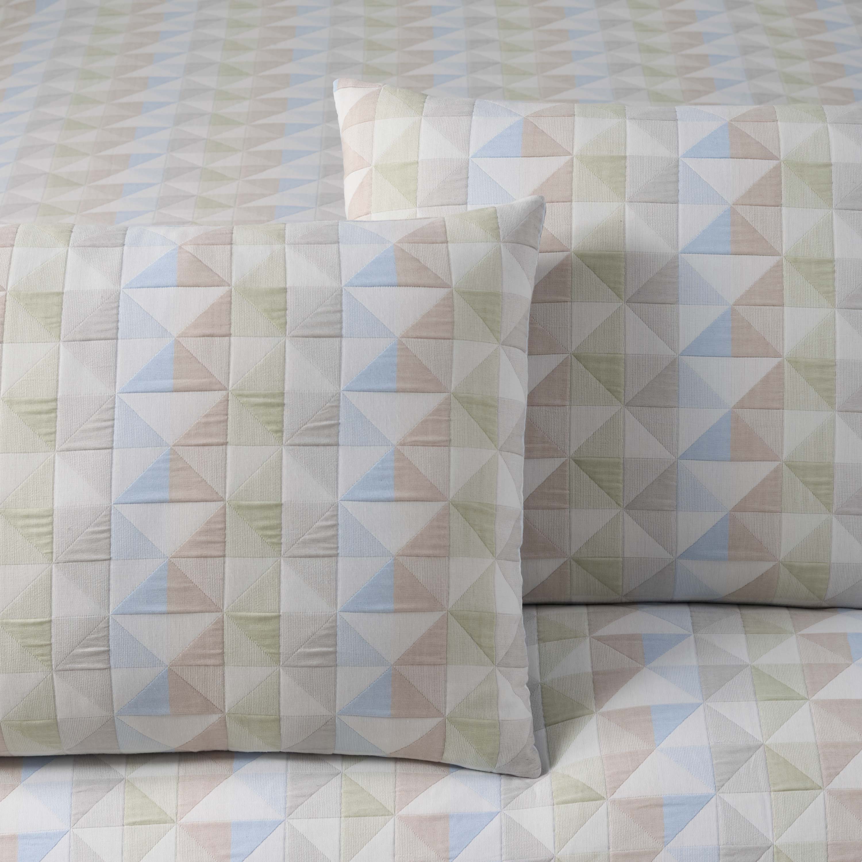 Comforter set featuring a geometric pattern of triangles in soft colors on a light background with matching pillow shams.