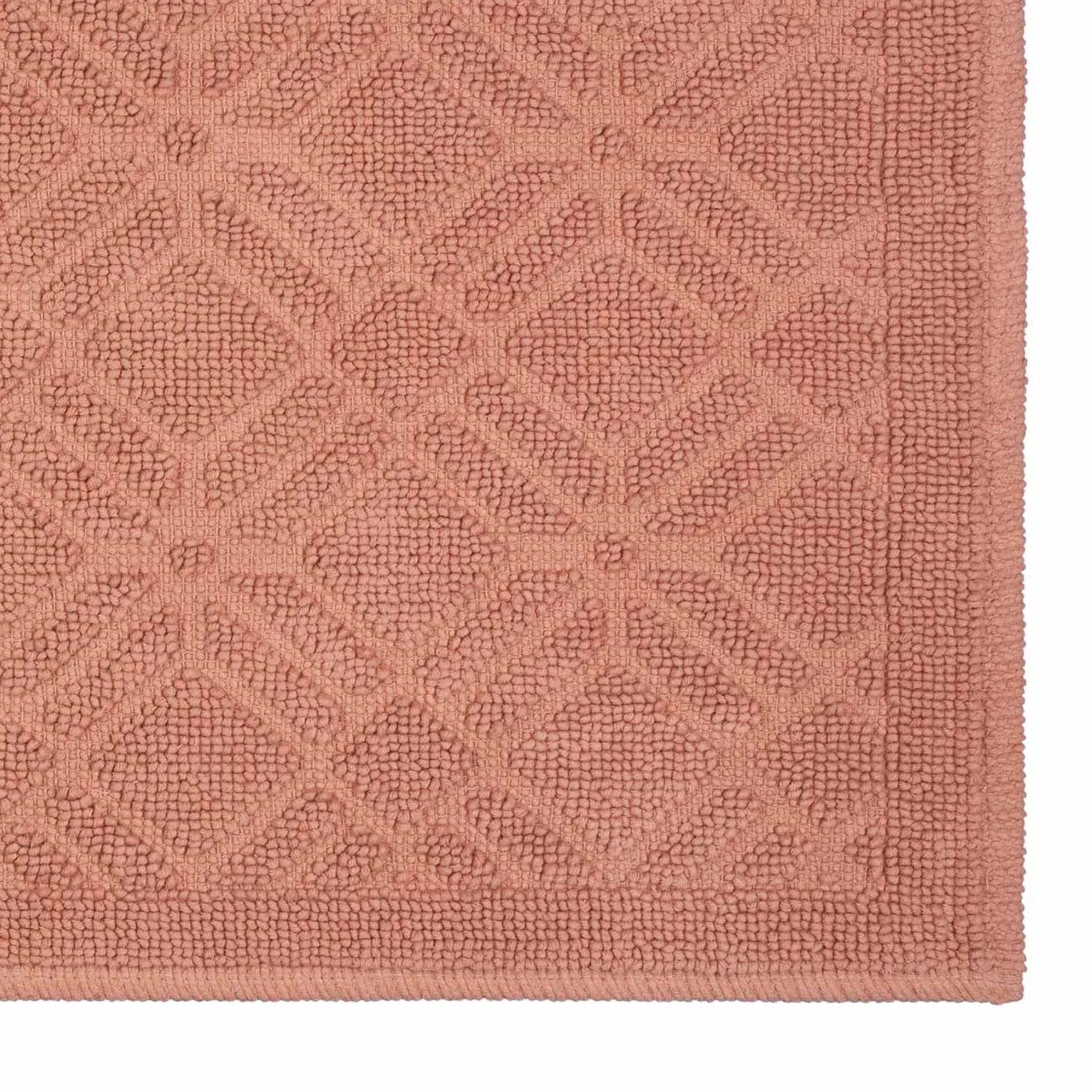 Textured bath rug in a soft pink hue featuring a geometric pattern.