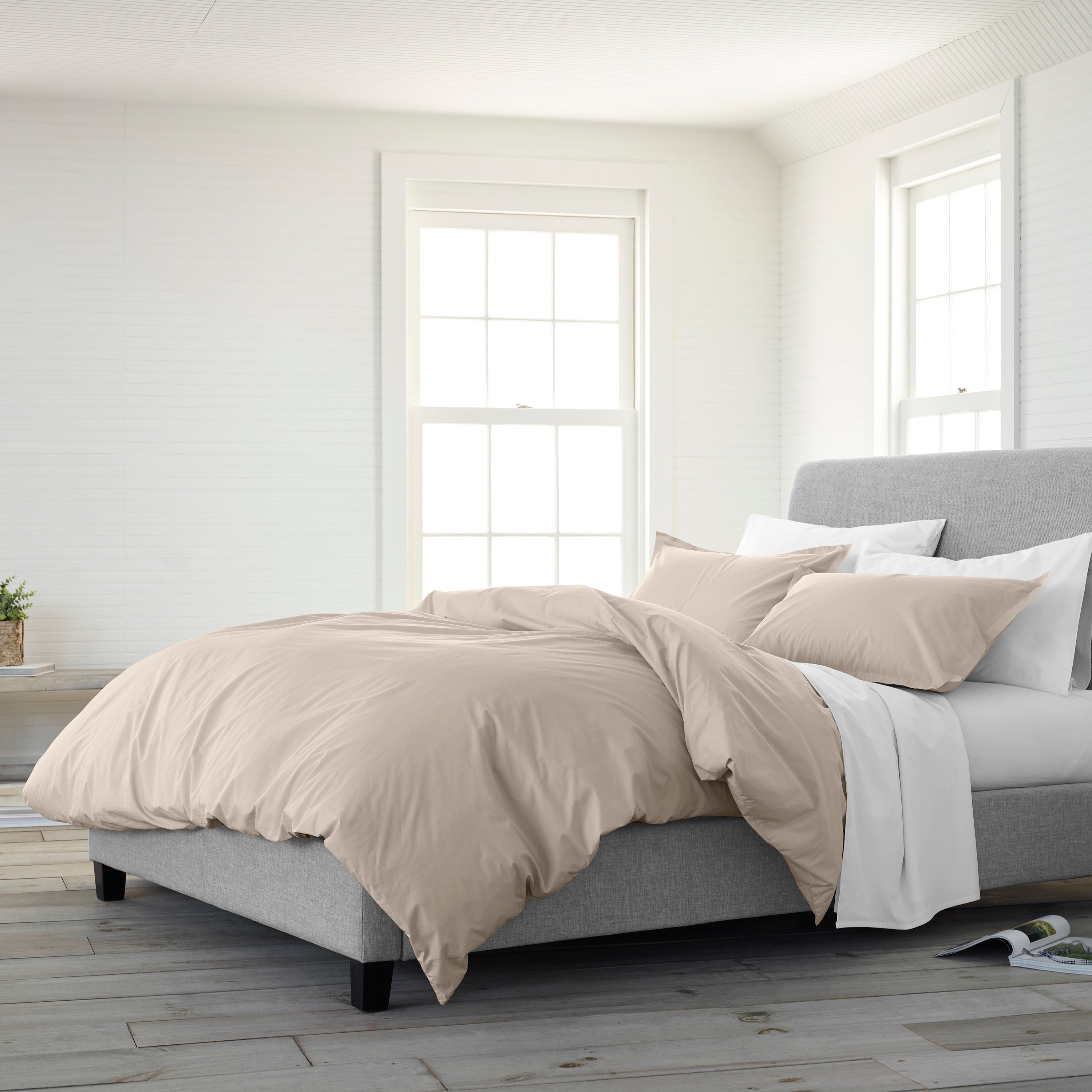 Beige duvet set on a gray upholstered bed with white and beige pillows in a bright, minimalist room.