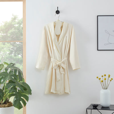Satin robe in cream color with a matching eyemask, hanging on a hook against a white wall.