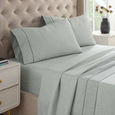 Light gray herringbone sheet set displayed on a bed with two matching pillows and a nightstand beside it.