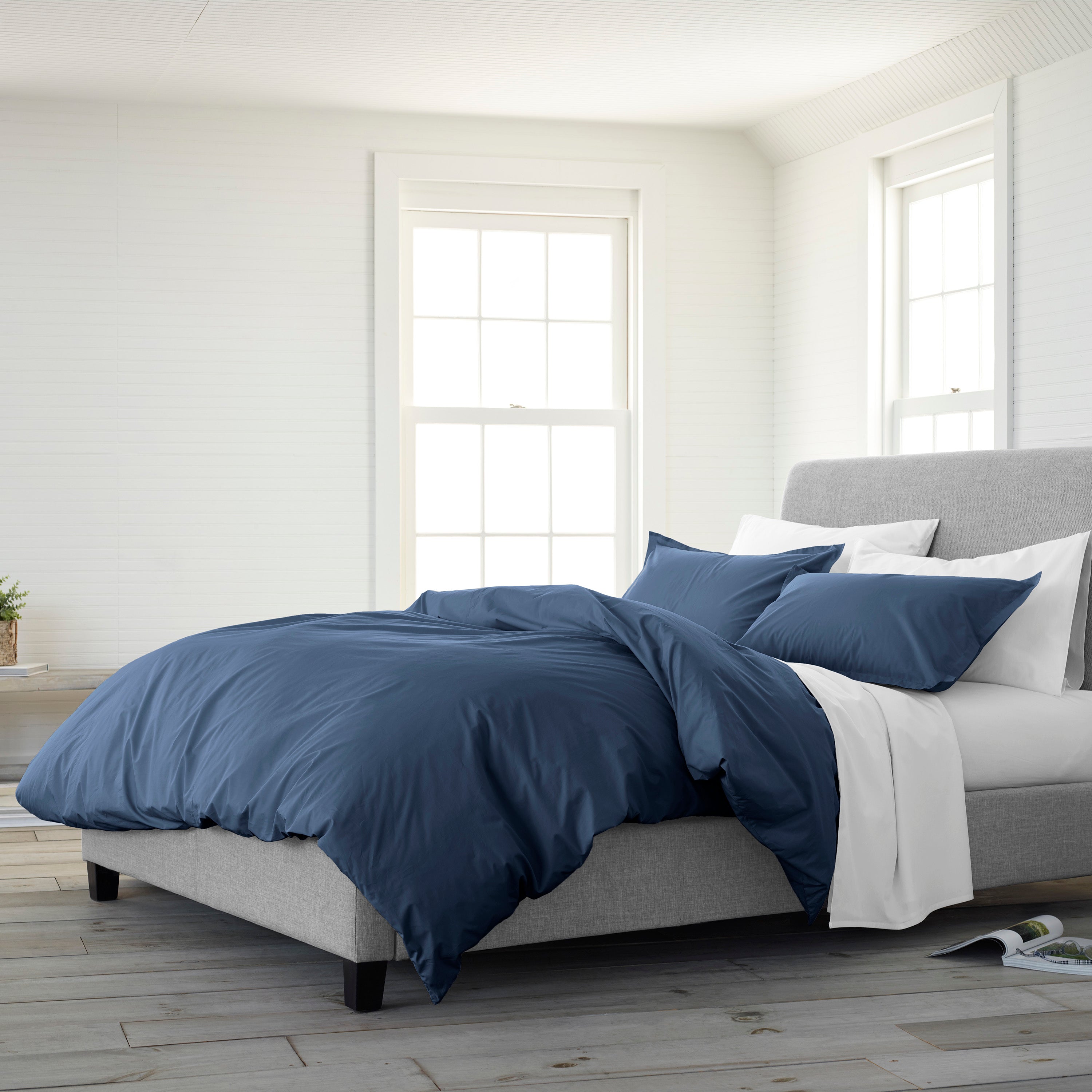 Navy blue duvet cover set with matching pillowcases on a light gray bed in a bright, airy room.
