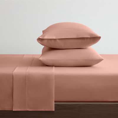 Solid pink cotton and Tencel sheet set with two stacked pillows on a bed.