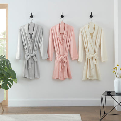 Three satin robes in gray, pink, and cream hanging on hooks, each with a matching eyemask.