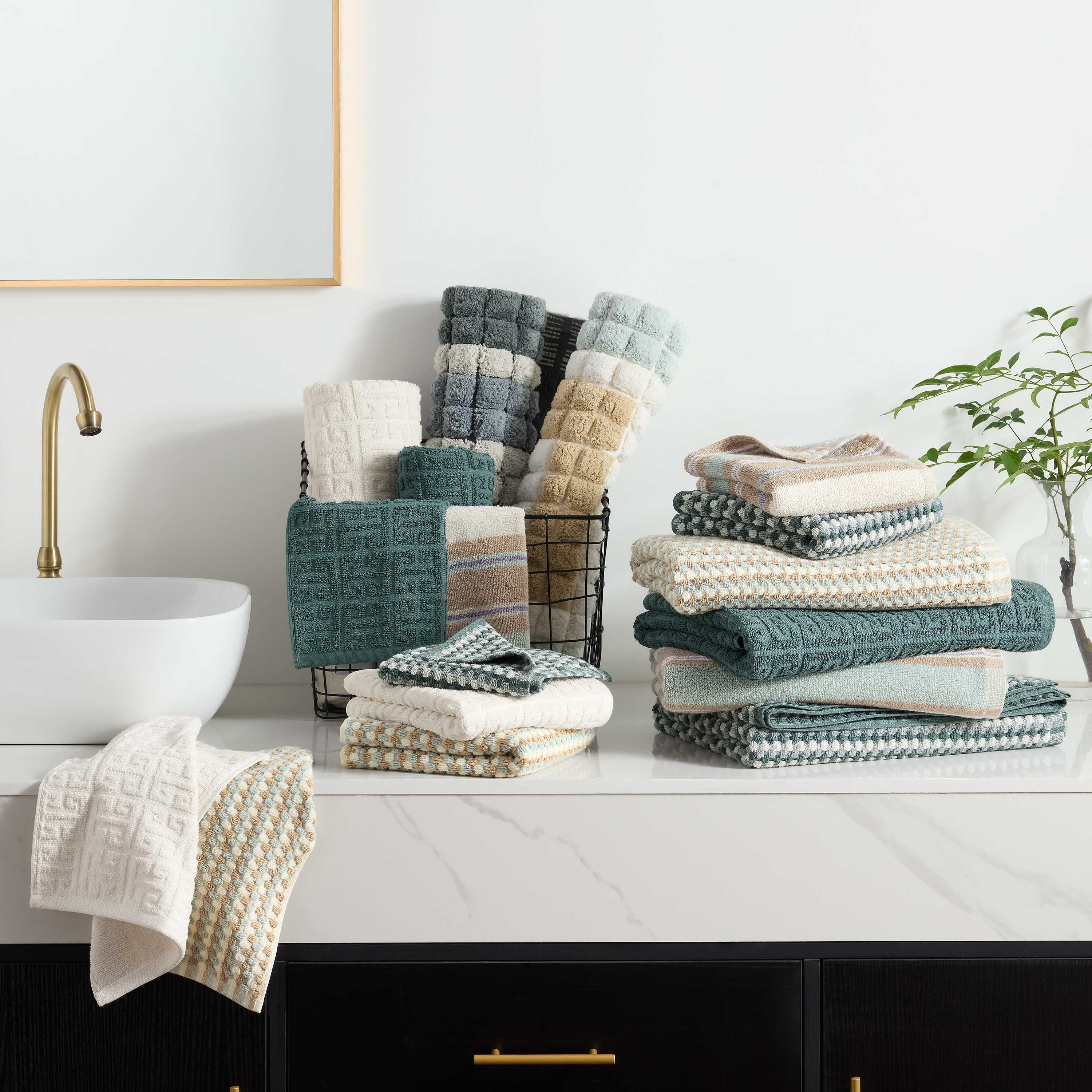 Two hand towels in various colors displayed on a countertop with a sink and decorative plant in the background.