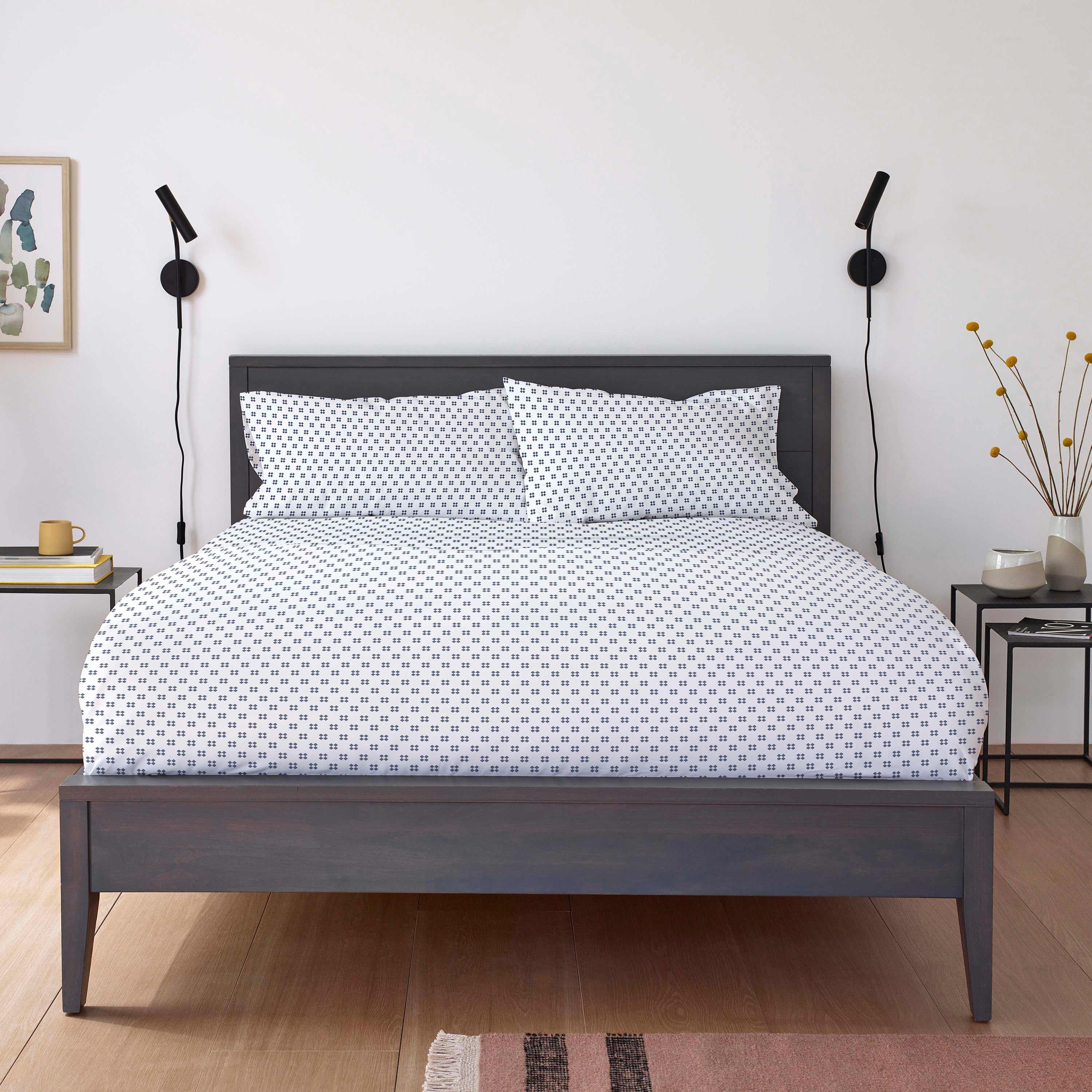 White bed with a patterned sheet set and matching pillows, framed by a dark wooden headboard and bedside tables.