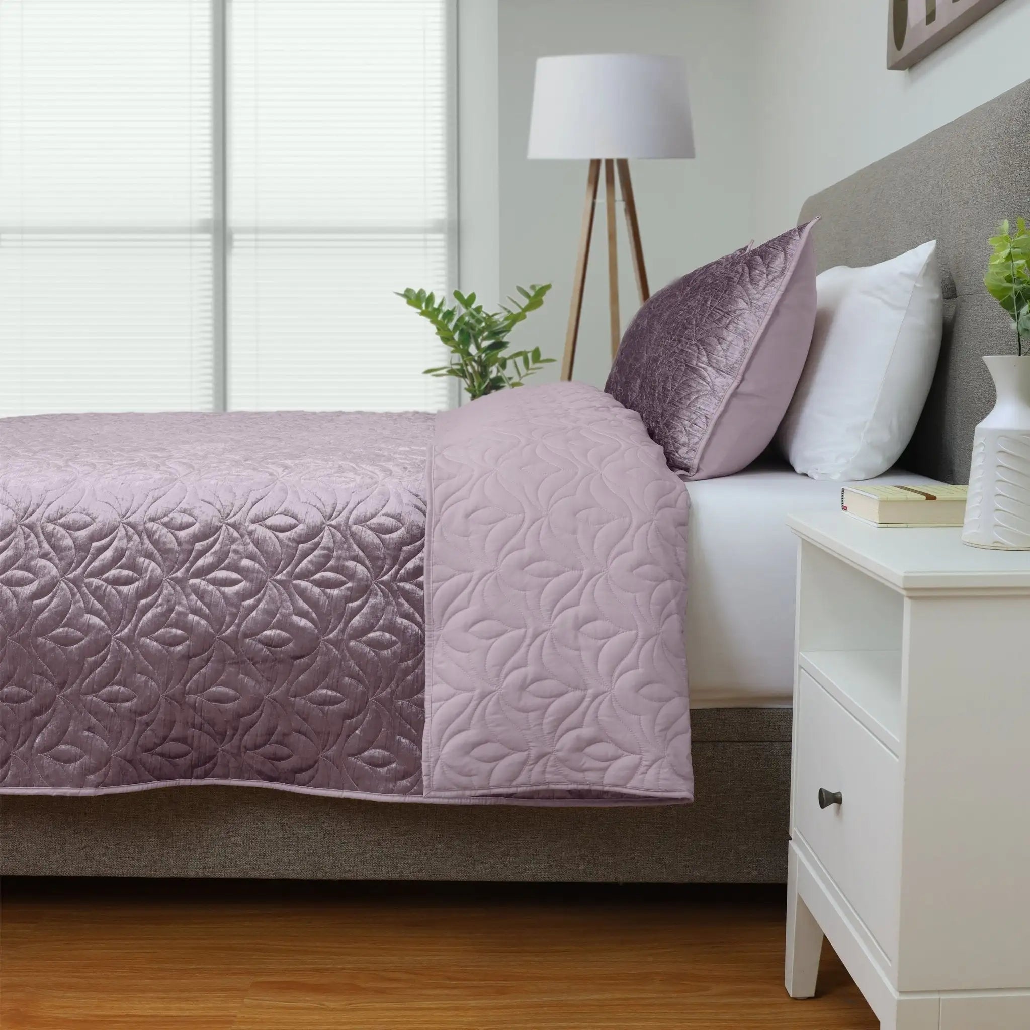 Bedroom with a bed covered in a purple quilt and pillow shams.