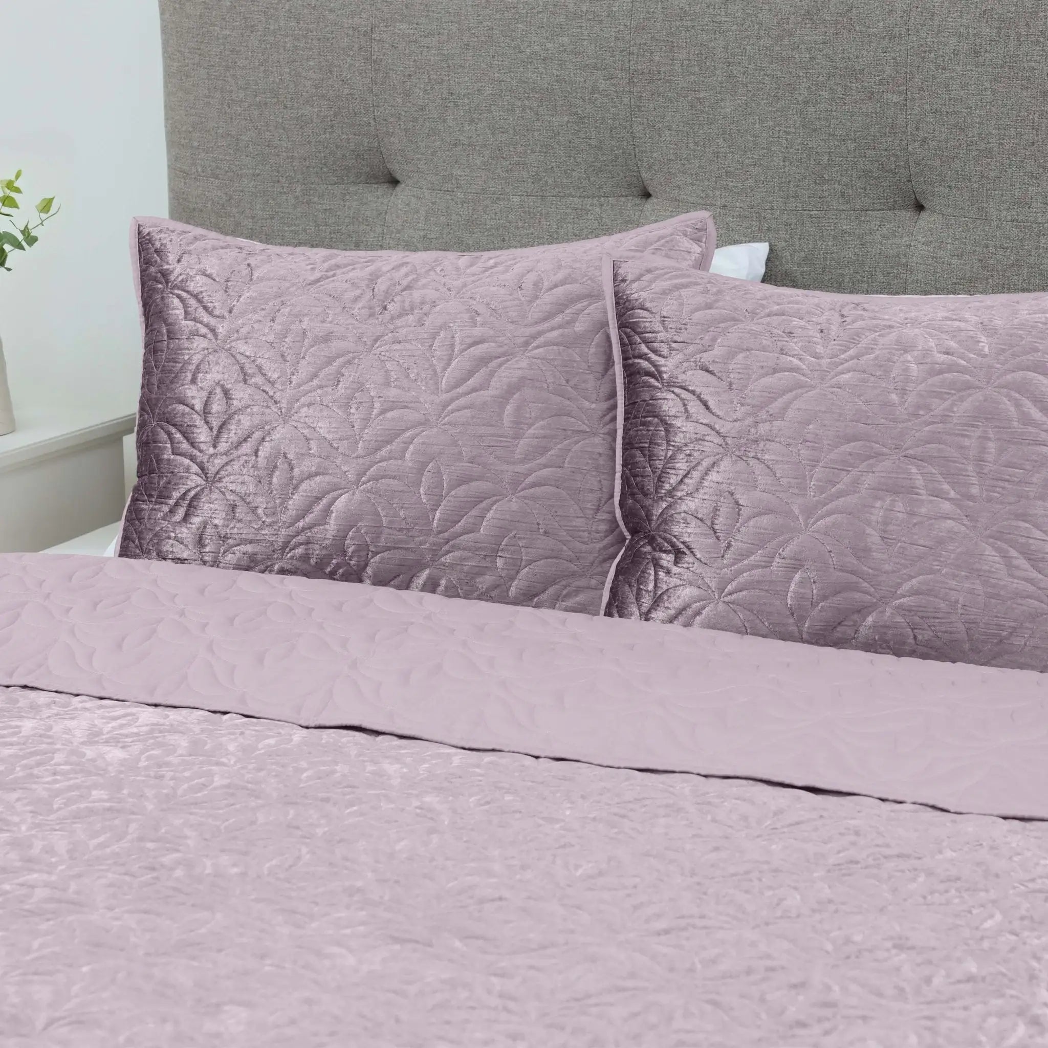Purple quilted bedding set on a bed with a gray upholstered headboard.