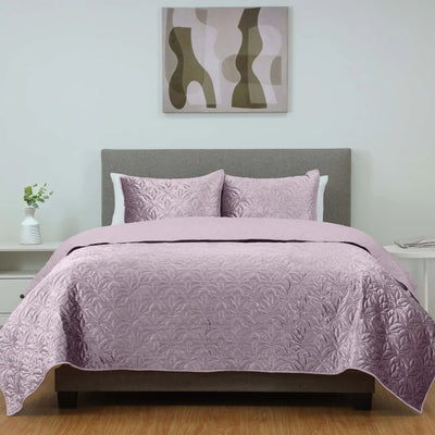 A purple quilt set with matching pillow shams on a bed with a gray upholstered headboard.