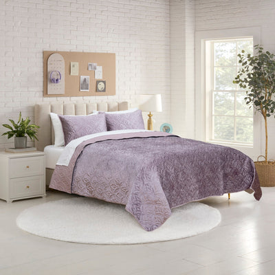 Bedroom with a bed covered in a purple quilt set.
