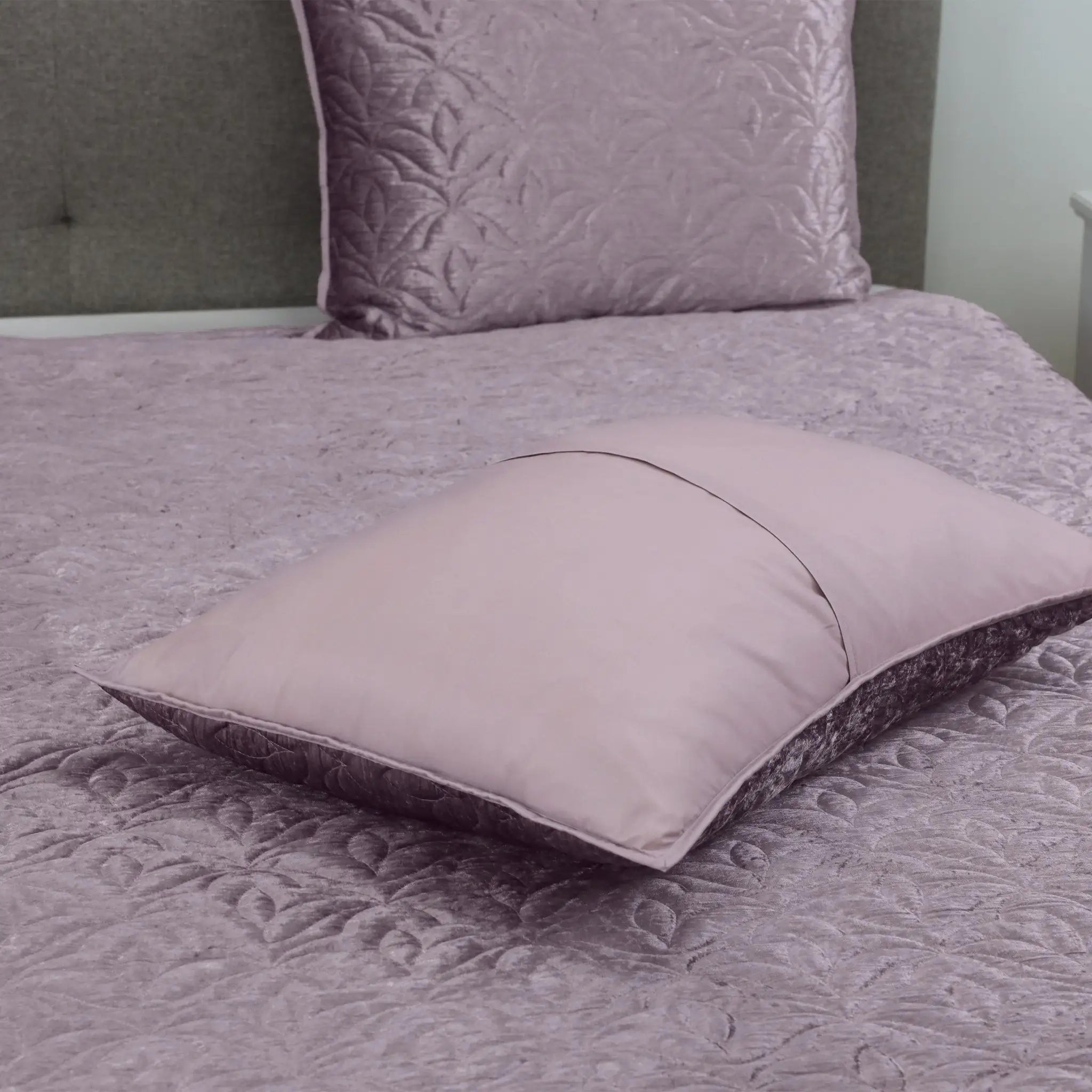 A purple pillow sham with a dark textured border resting on a matching purple quilt.