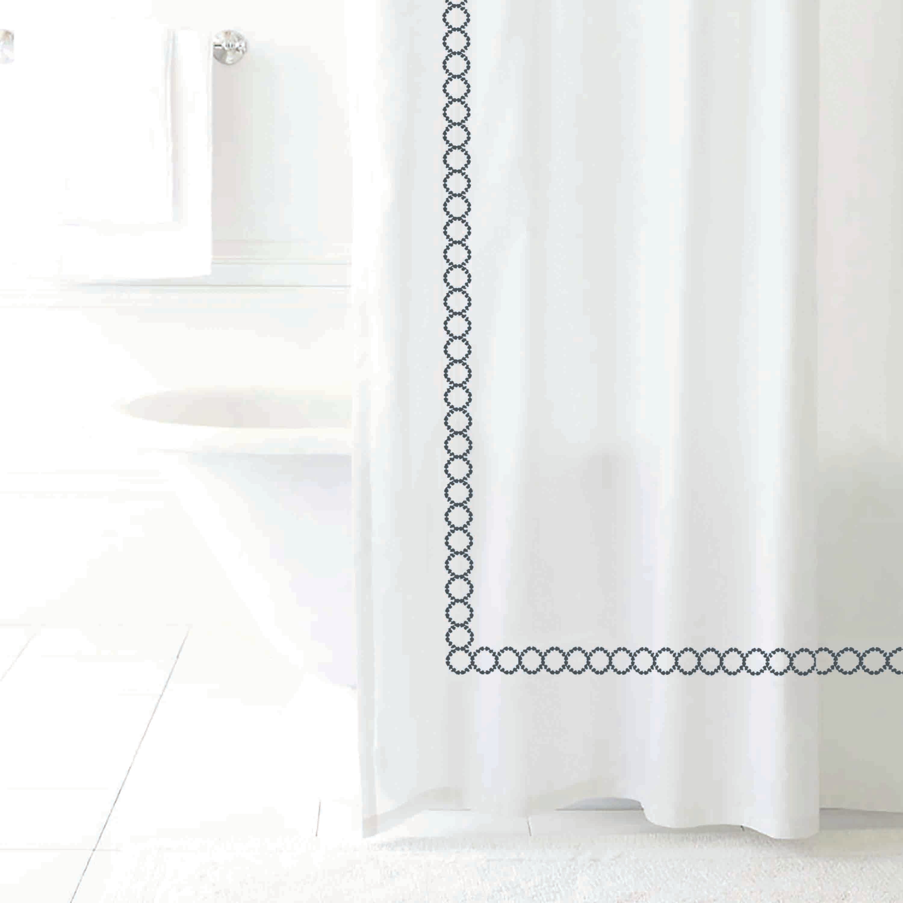 White shower curtain with a decorative navy circular border design, hanging in a bright bathroom setting.