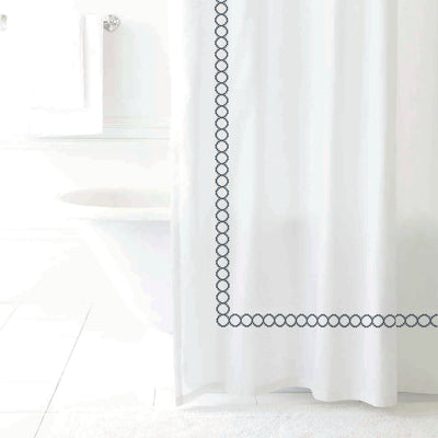 White shower curtain with a decorative navy circular border design, hanging in a bright bathroom setting.
