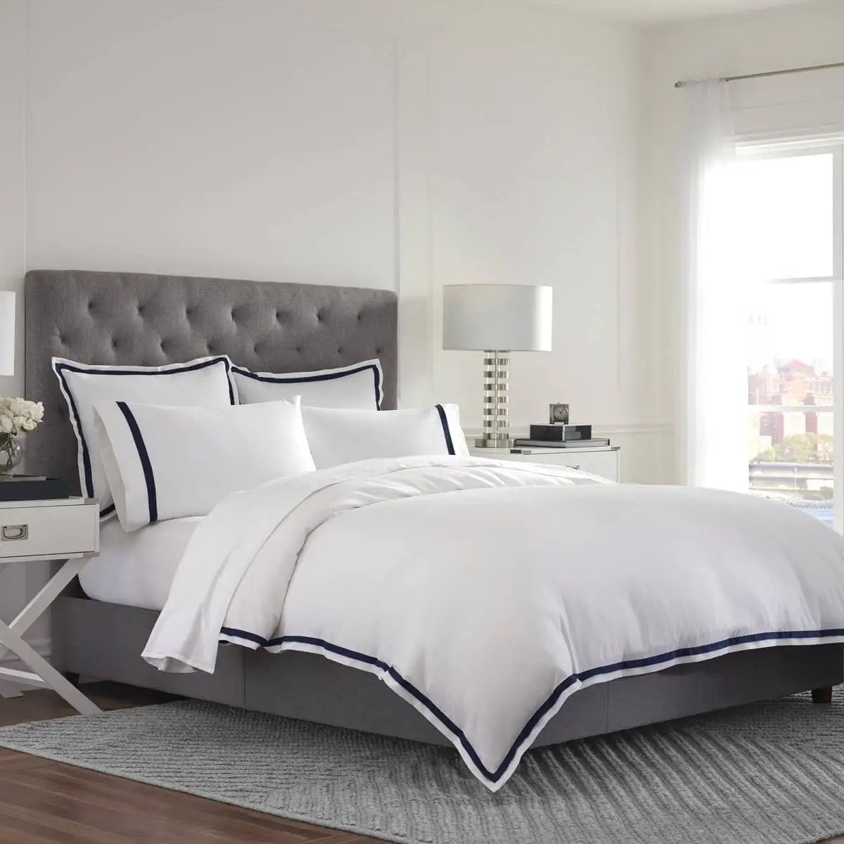 Bedroom with gray upholstered headboard and white duvet cover with navy trim
