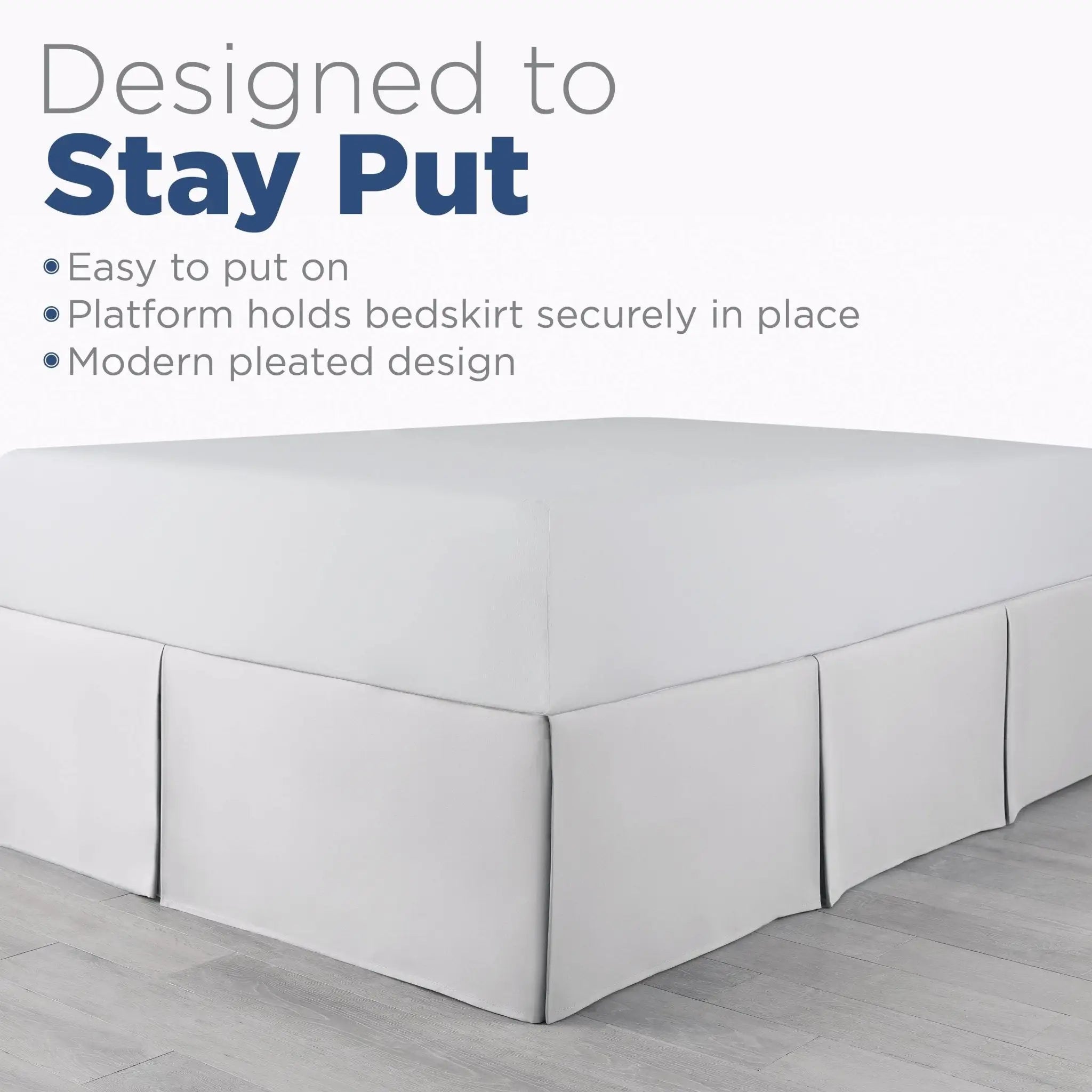 A white bed skirt fitted over a mattress on a bed frame, shown with marketing text that reads 'Designed to Stay Put' and bullet points about easy placement and a platform hold.