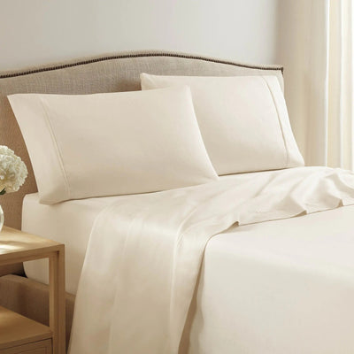Neatly made bed with ivory bedding and pillows in a bedroom setting.