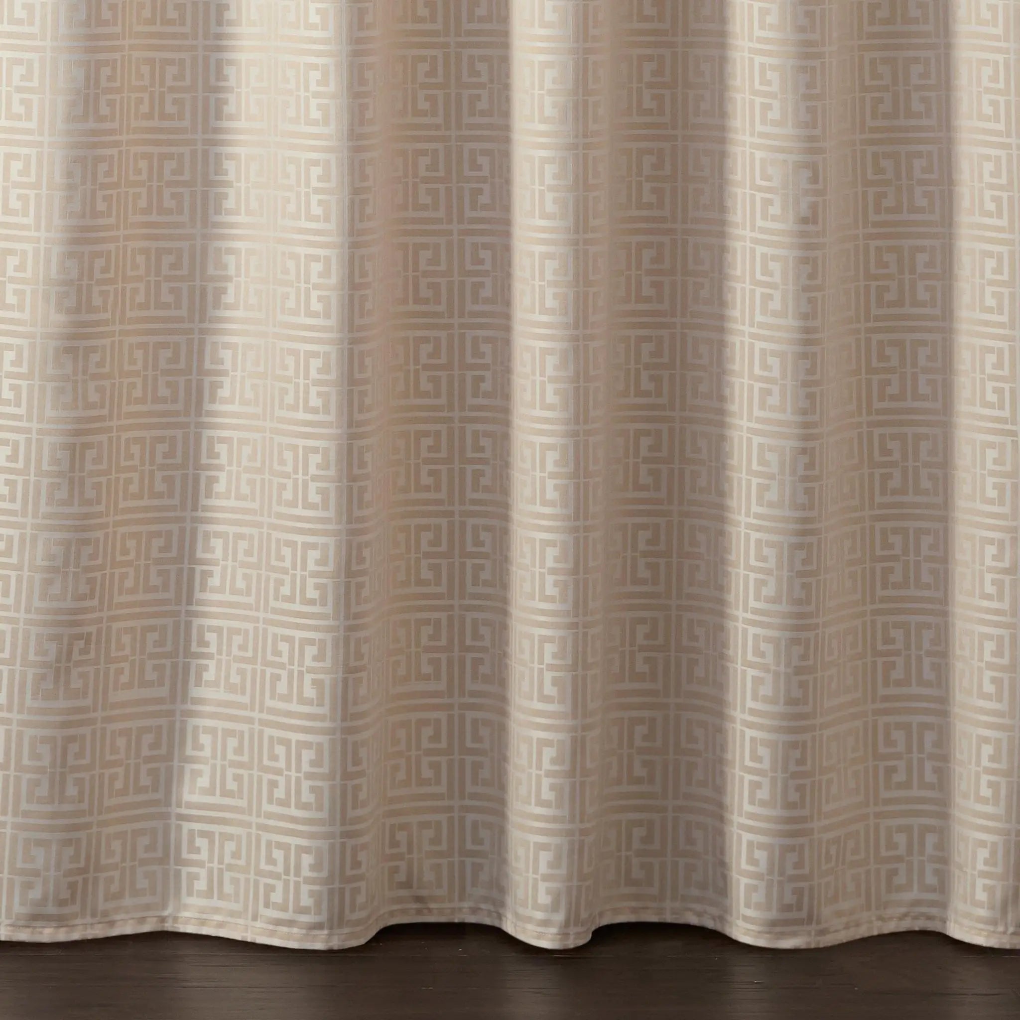 Beige curtain panel with a repeating geometric Greek key pattern in a light taupe, hanging over a dark wood floor.