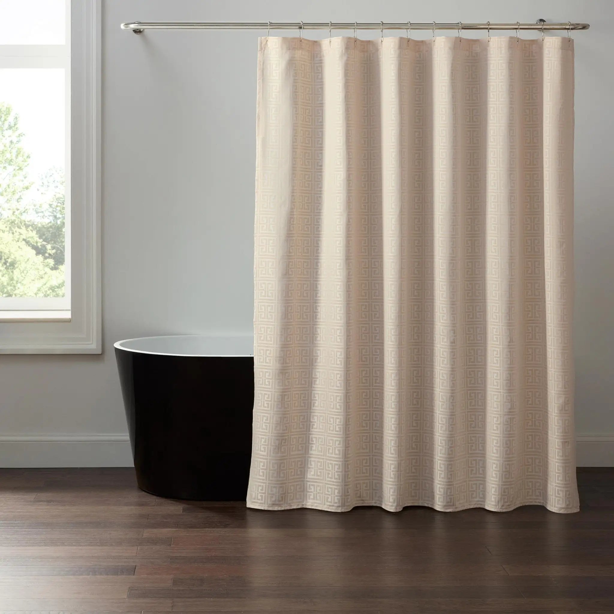 A textured cream-colored shower curtain hanging from a silver metal rod in a bathroom setting with a black freestanding bathtub and a window.