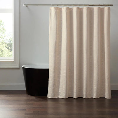 A textured cream-colored shower curtain hanging from a silver metal rod in a bathroom setting with a black freestanding bathtub and a window.