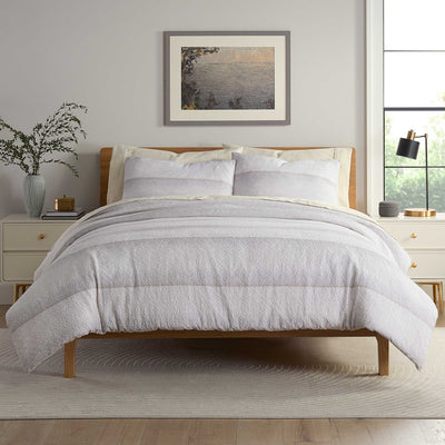 Neatly made bed with light gray comforter set in a bedroom setting.