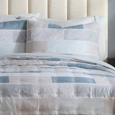 Patterned quilt set on a bed against a neutral headboard.