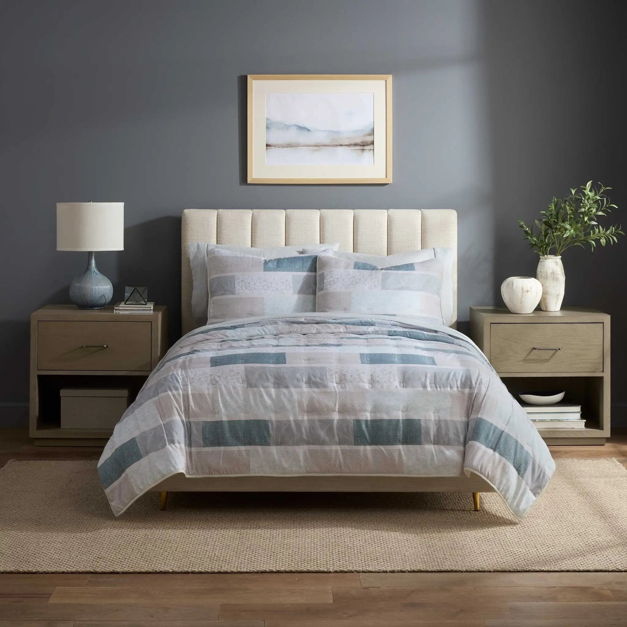 A neatly made bed in a bedroom setting, featuring a striped quilt in shades of blue, gray, and white, matching striped pillows shams.