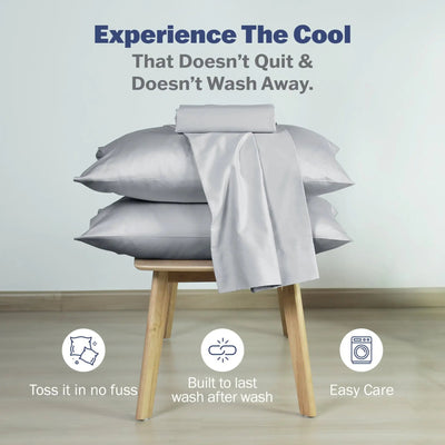 A stack of light gray pillowcases with a matching gray sheet draped over the top. Blue text at the top reads, 'Experience The Cool That Doesn't Quit & Doesn't Wash Away.