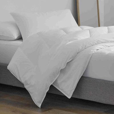White bedding set including a duvet cover and pillows on a bed with a gray upholstered base, shown in a minimalist bedroom setting.