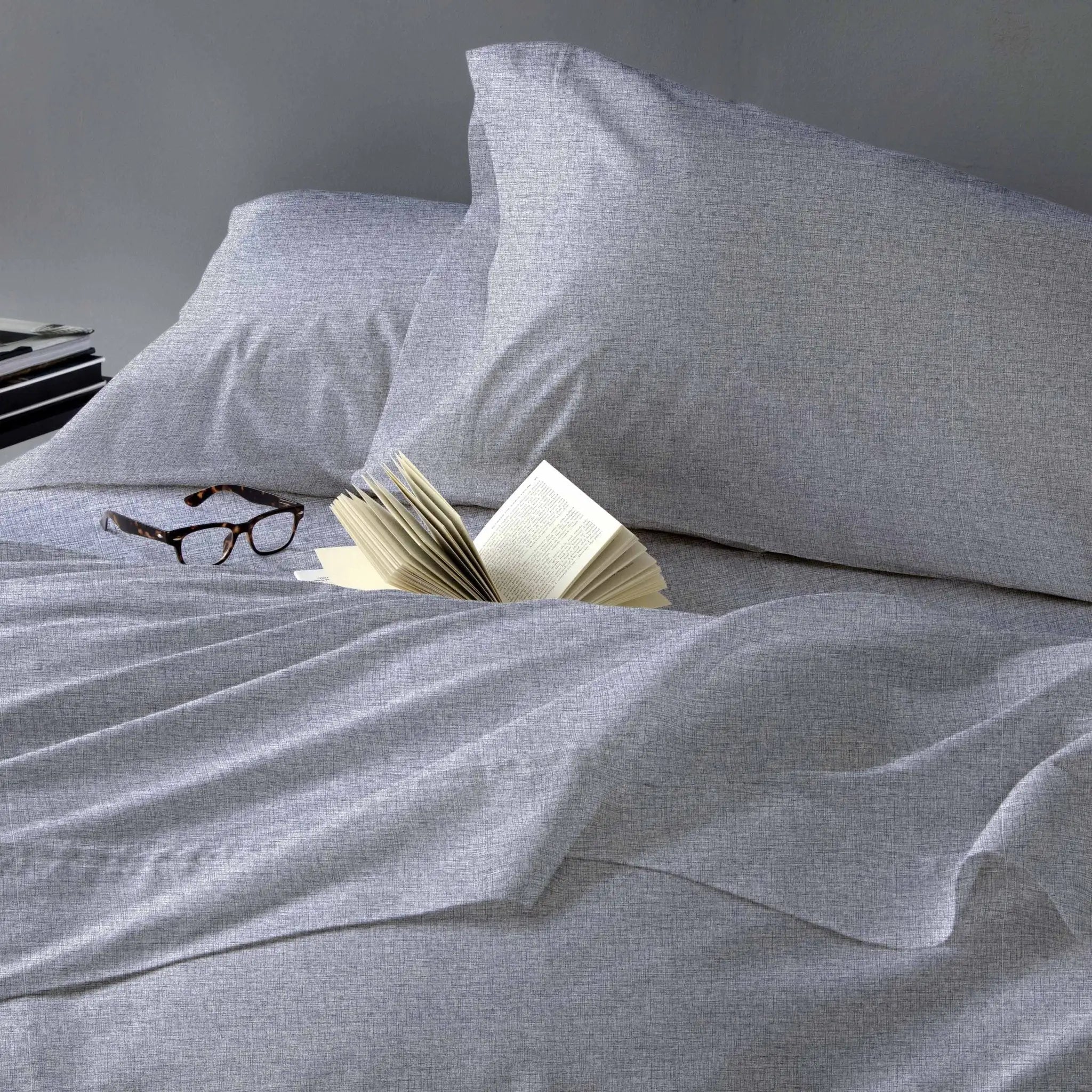 Gray bedding set with an open book and glasses on a bed.
