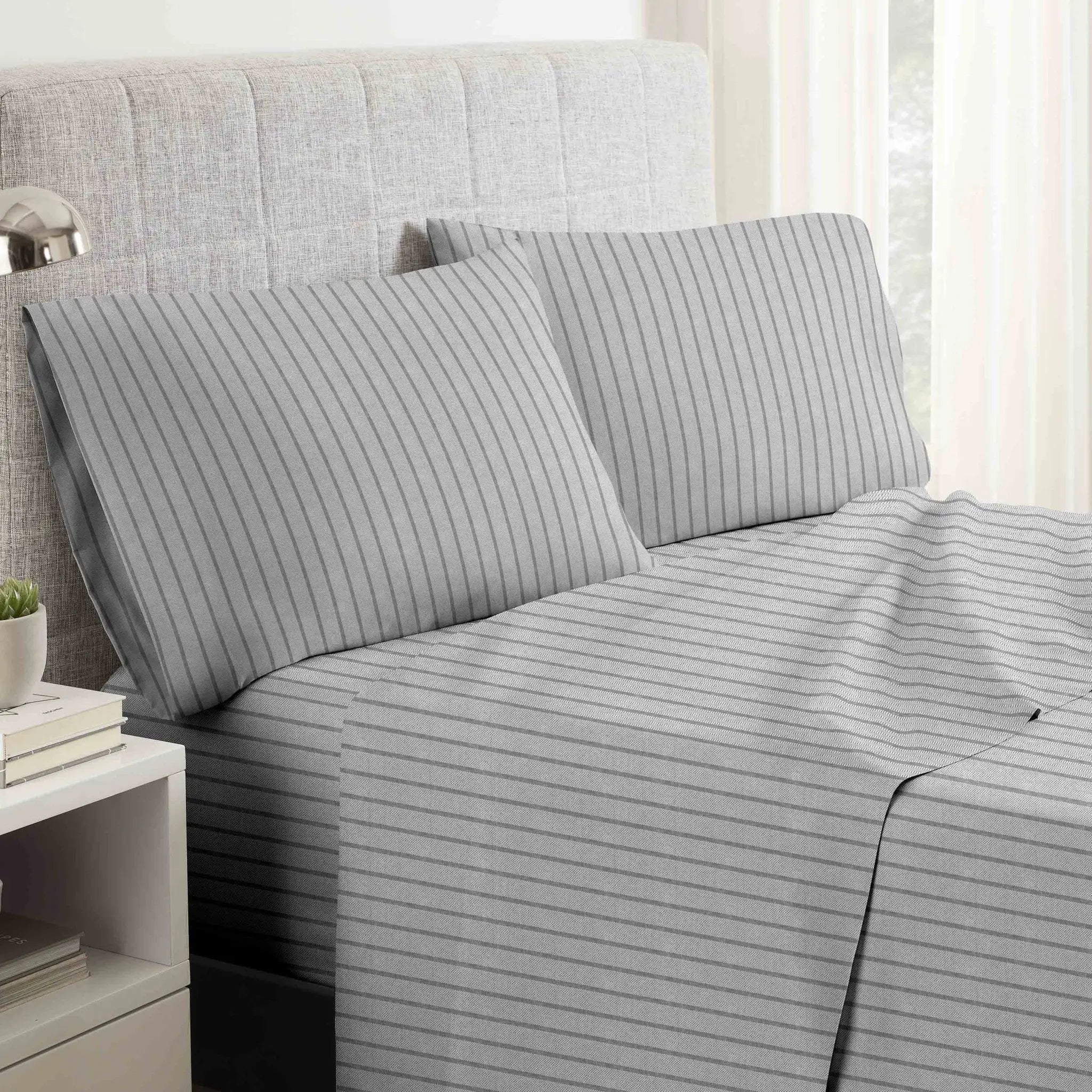 Gray striped bed sheets on a neatly made bed with pillows.