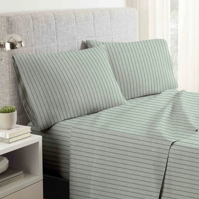 A bed dressed in a light sage green sheet set with thin vertical dark green stripes, styled with two matching pillowcases in front of a gray upholstered headboard.
