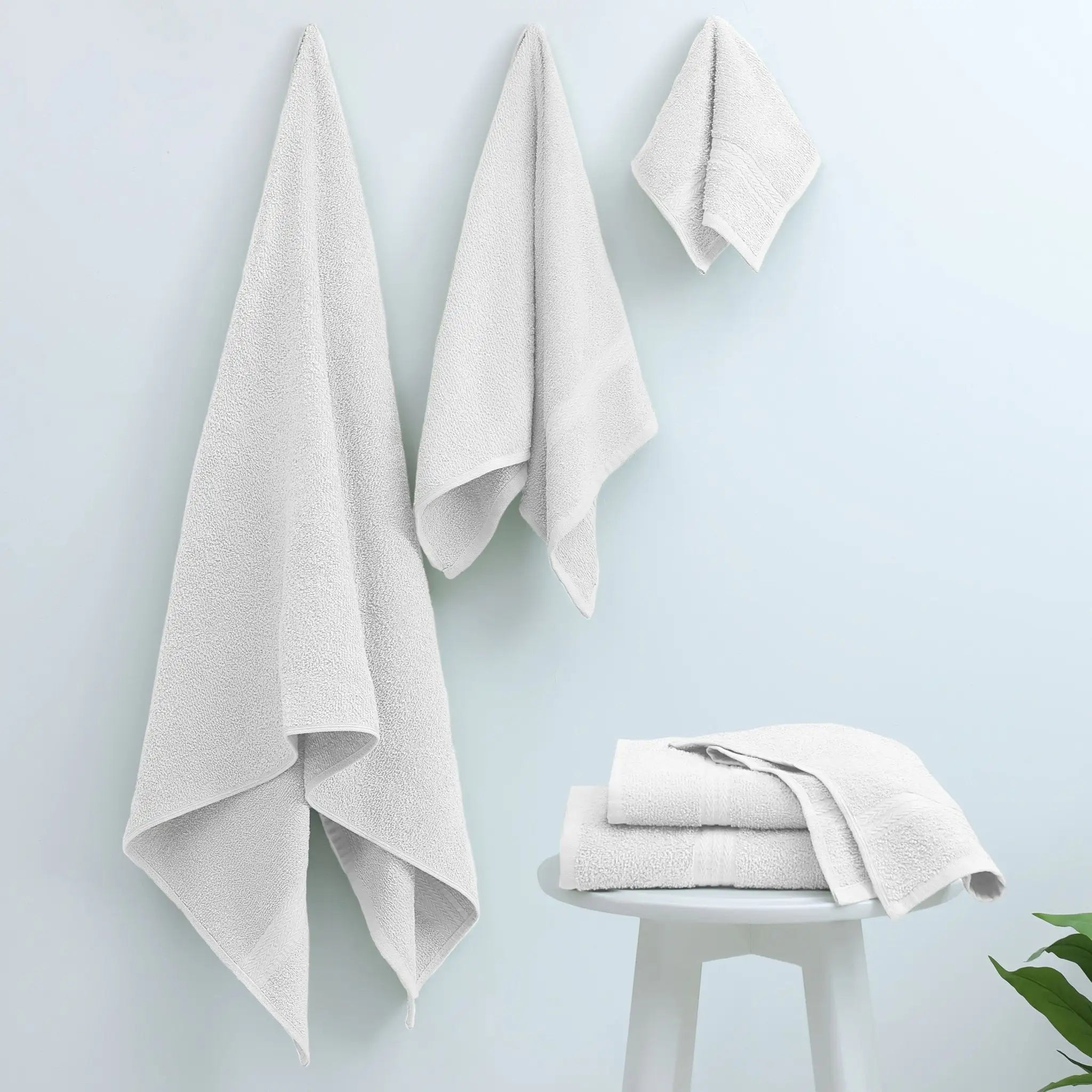 Three white cotton towels hanging on a pale blue wall.
