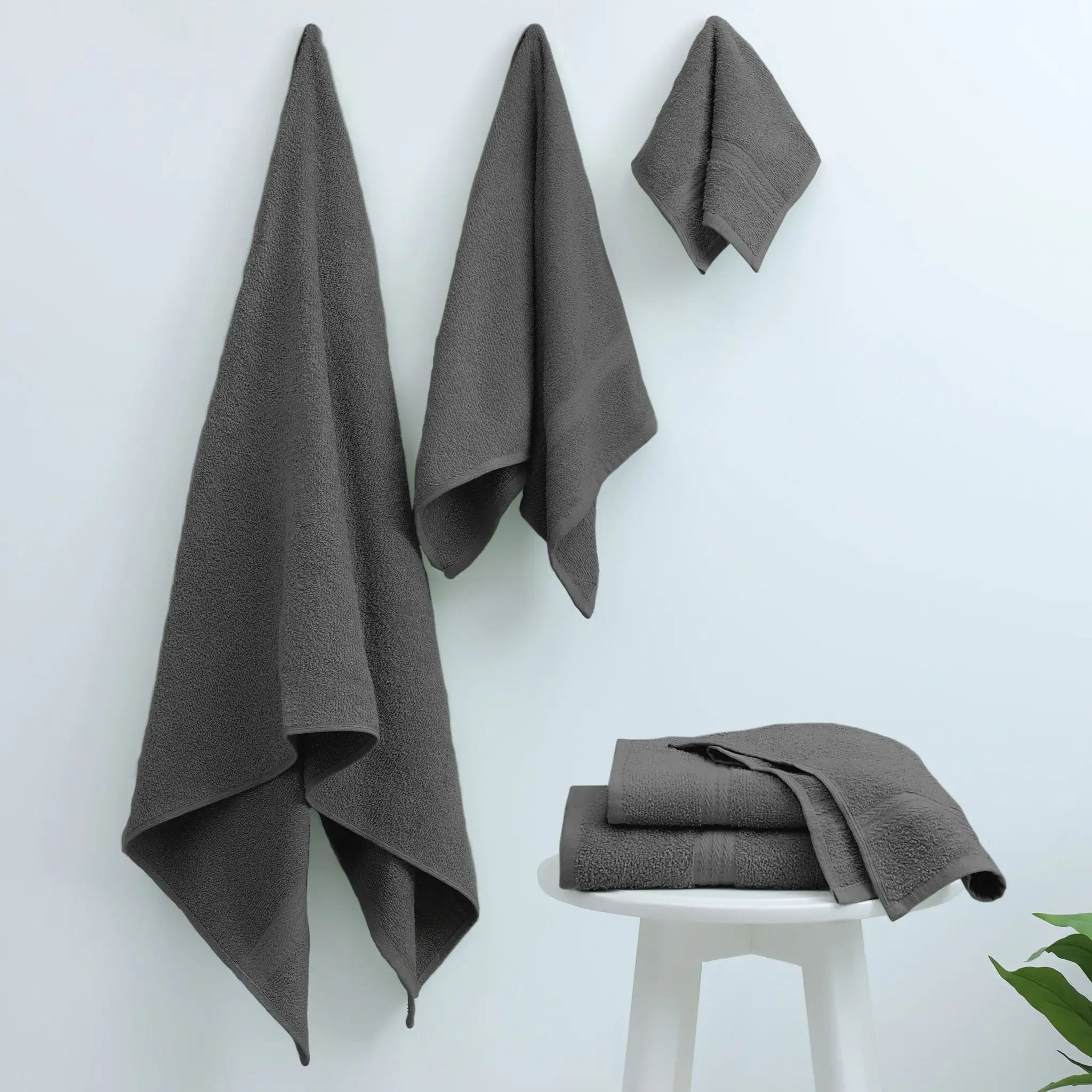 Charcoal towels hanging on a white wall with one folded on a stool.