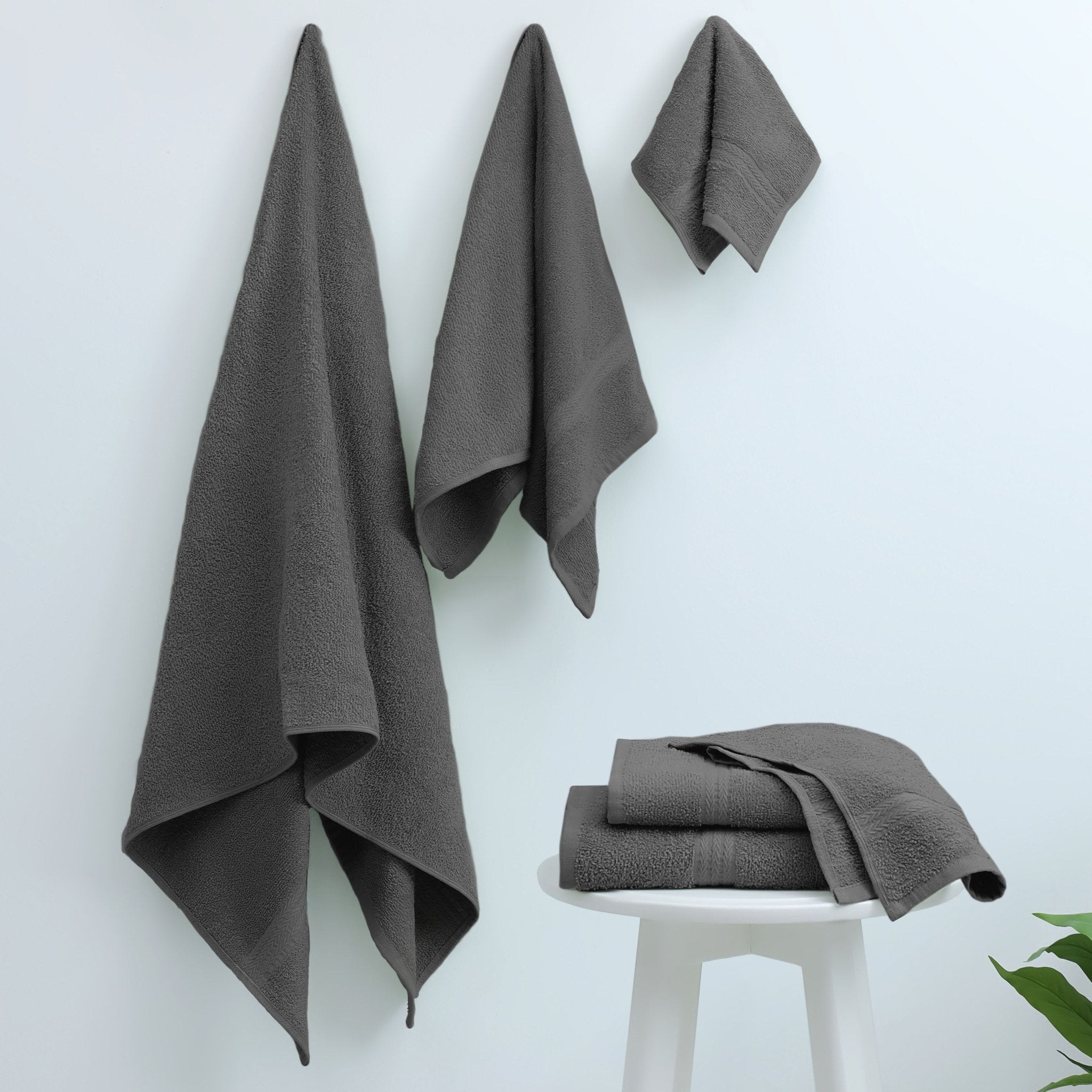 Dark gray towels hanging on a white wall with one folded on a stool.