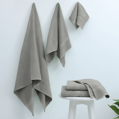 Set of gray towels on a white surface with a plant in the corner