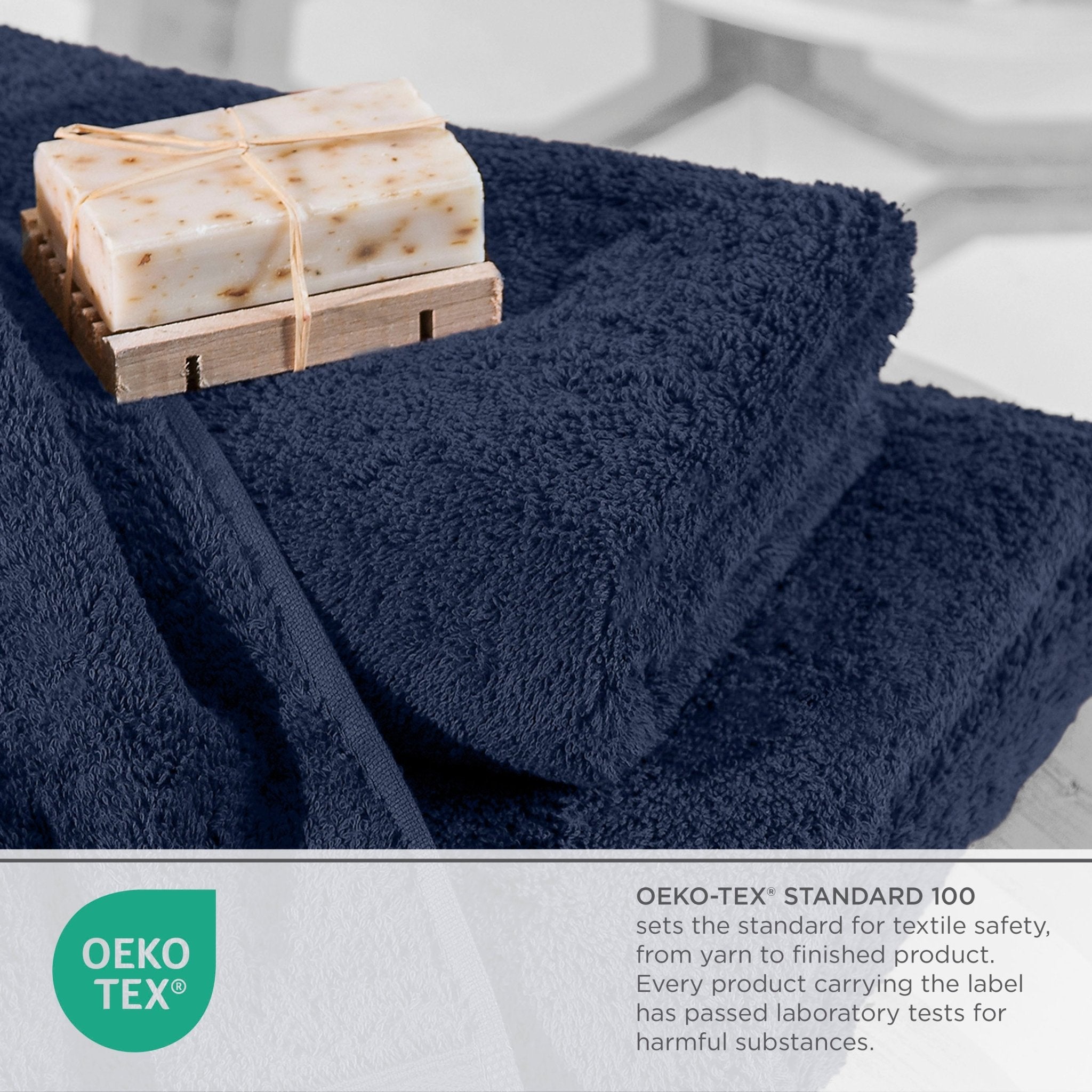 Navy blue towels with soap on a wooden holder on a light gray background, featuring Oeko-Tex logo.