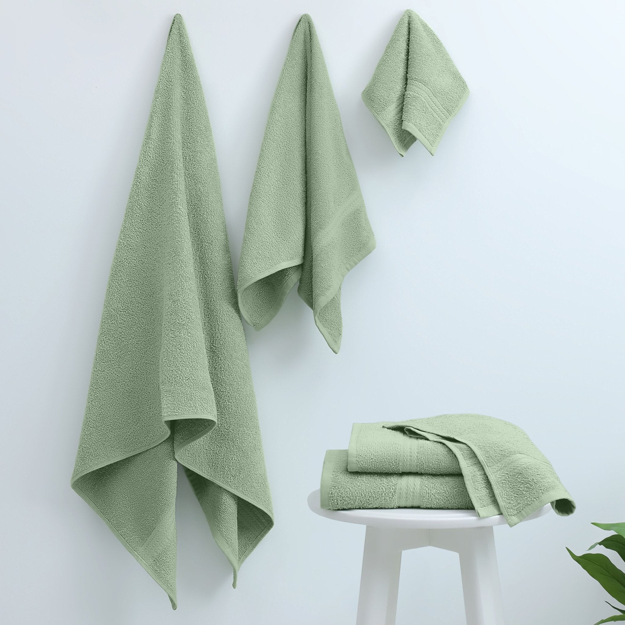 Green towels on a white surface with a plant in the corner