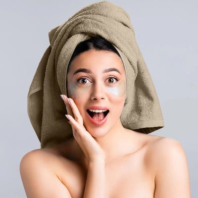 A woman with a beige towel wrapped around her head and eye patches under her eyes.