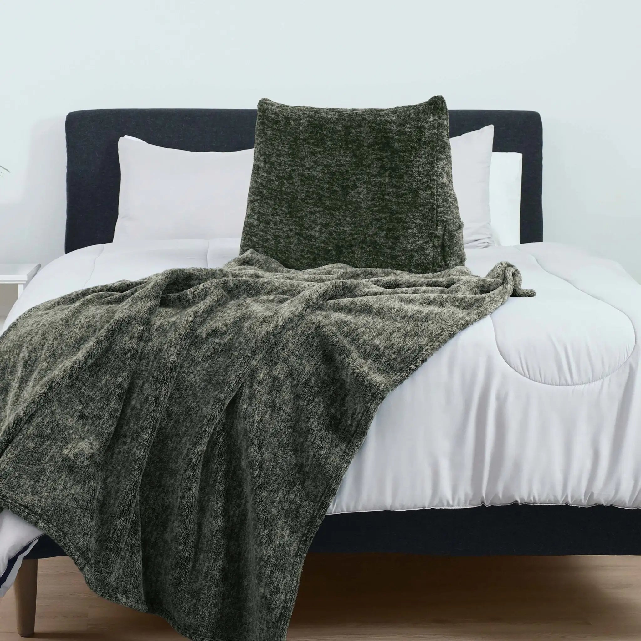 A dark olive green textured throw blanket and matching pillow are styled on a bed with white bedding and a dark headboard.