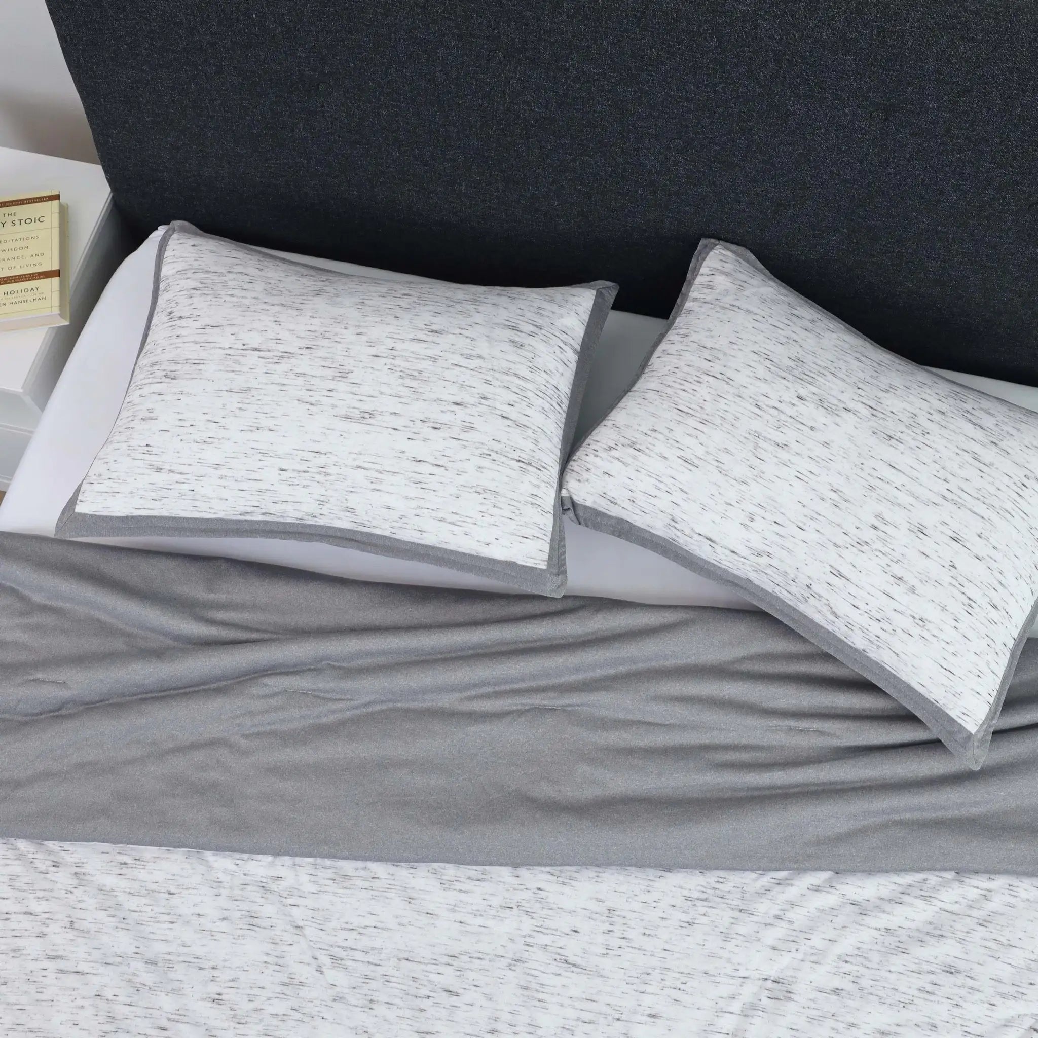 Two gray pillow shams on a bed with a dark headboard.