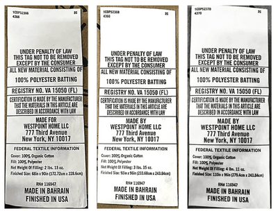 Three narrow vertical labels or tags showing the same printed text block, photographed against a dark background. The text reads 'UNDER PENALTY OF LAW THIS TAG TO BE REMOVED EXCEPT BY THE CONSUMER' and includes manufacturer and country-of-origin details such as 'Made for Westpoint Home LLC' and 'Finished in Bahrain.
