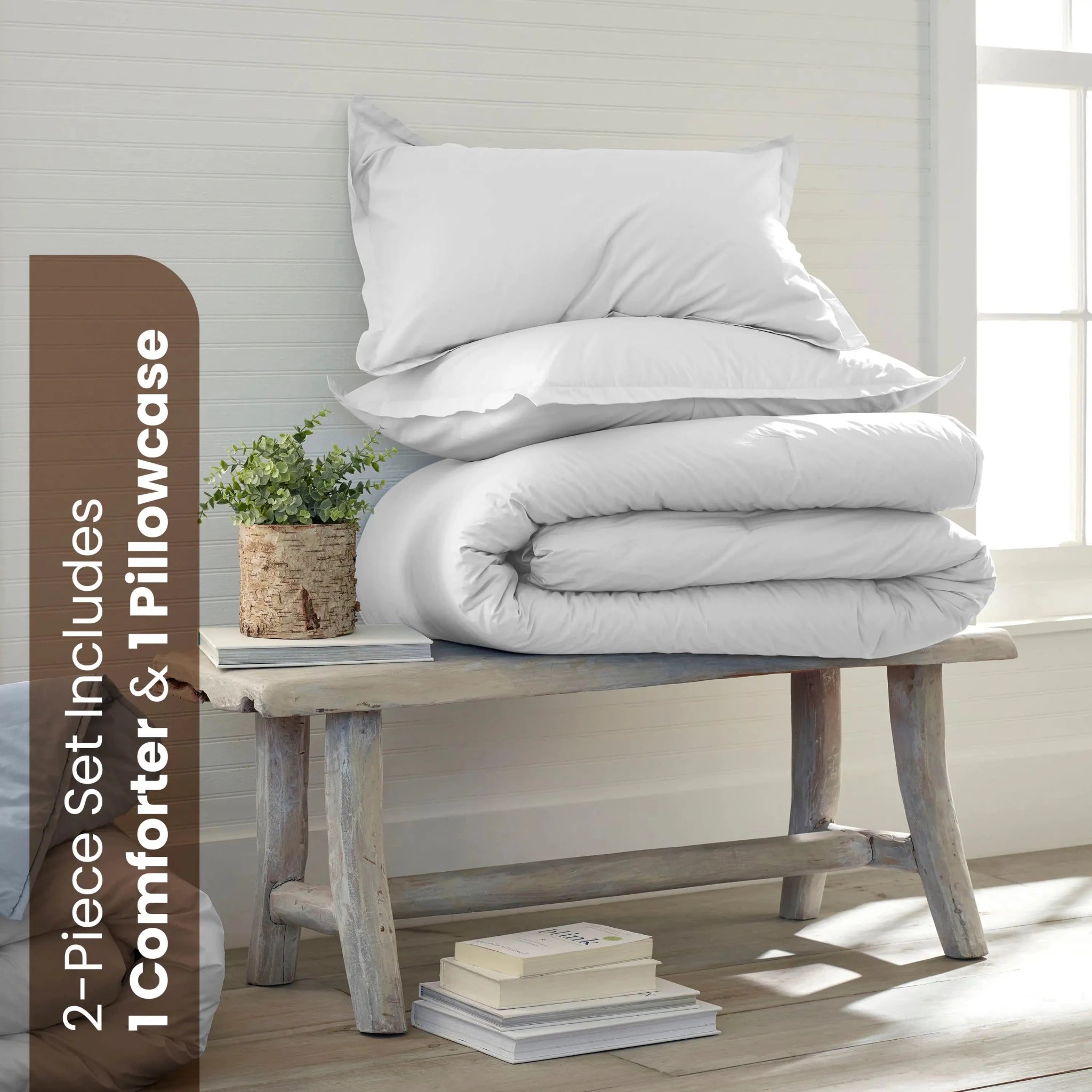 A bedding set displayed in a bright room. The set includes a folded white comforter and one white pillowcase.