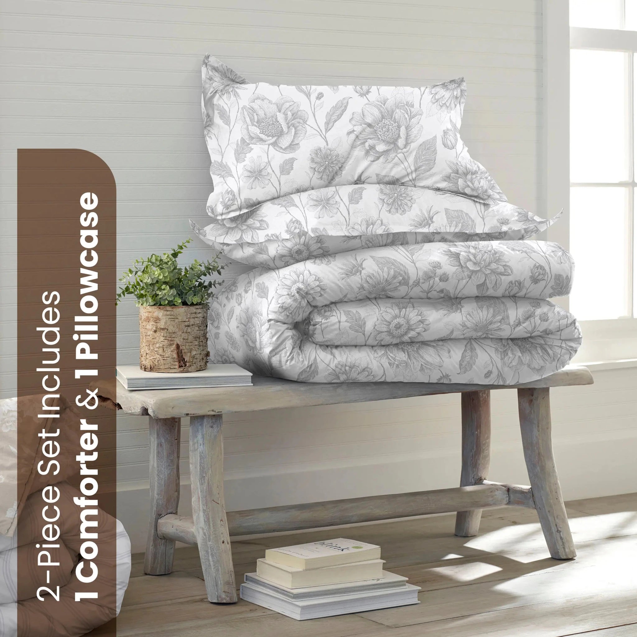 A bedding set displayed on a rustic wooden bench in a bright room. The set includes a white comforter and one matching pillowcase with a gray floral pattern.