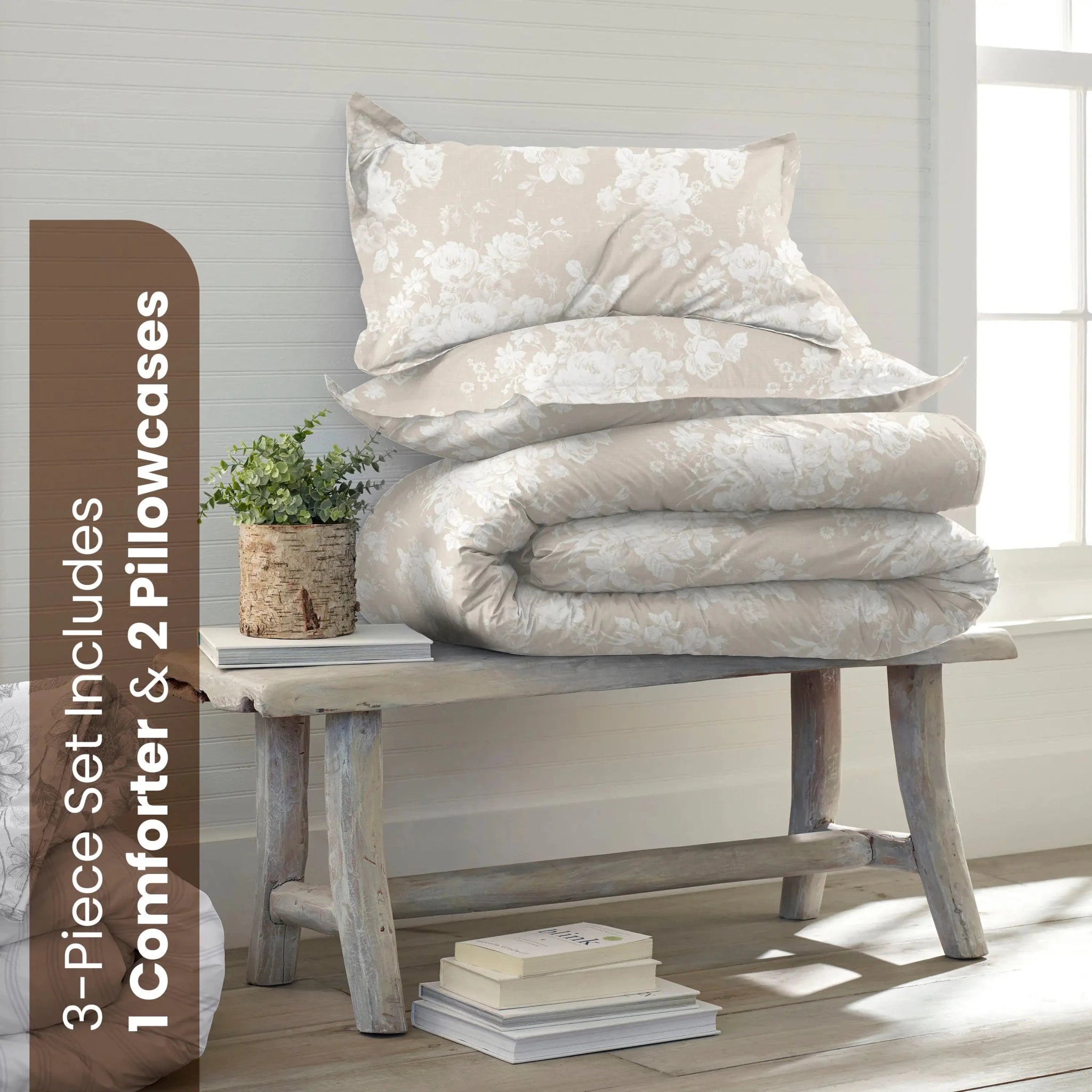 A bedding set displayed on a rustic wooden bench in a bright room. The set includes a light beige comforter with a white floral damask pattern and two matching pillowcases.