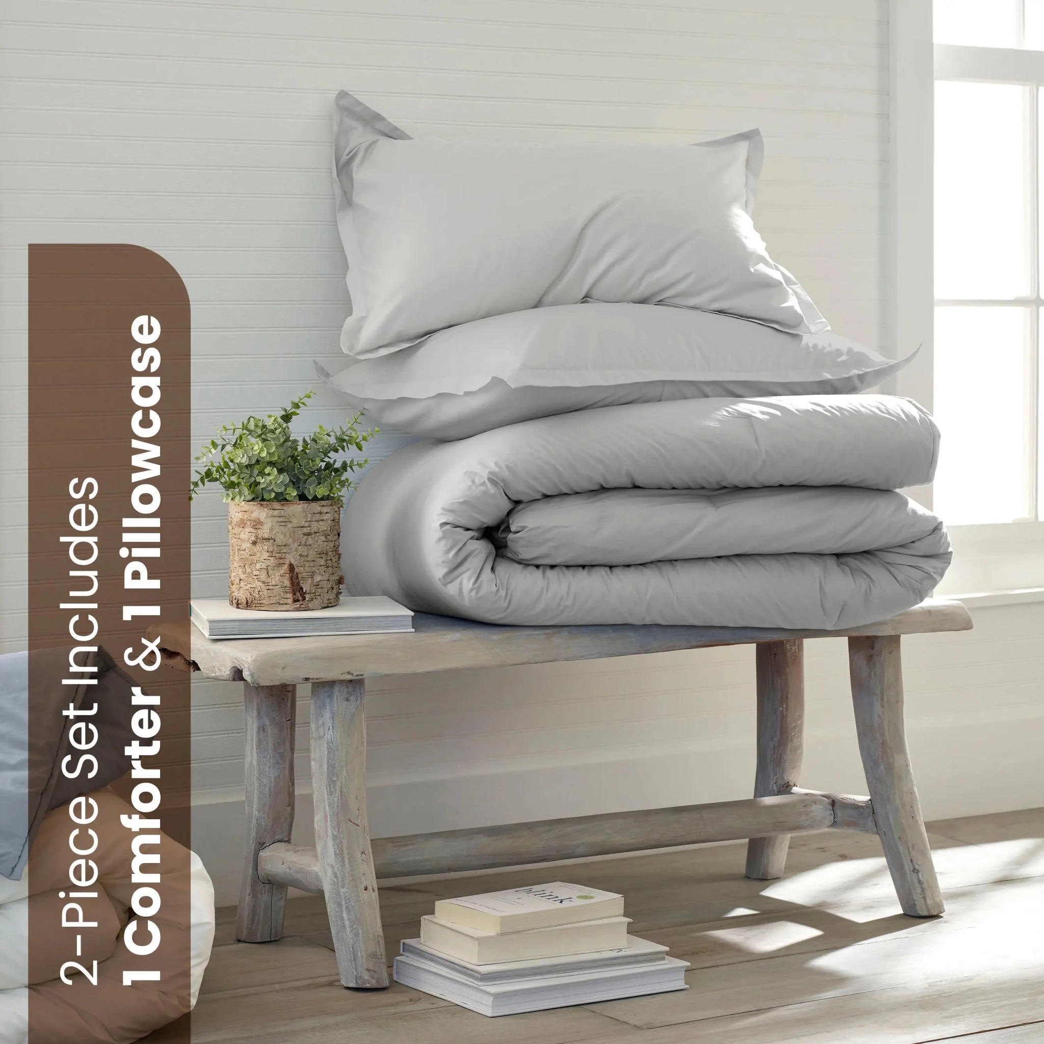 A bedding set displayed in a bright room. The set includes a folded light grey comforter and one white pillowcase.