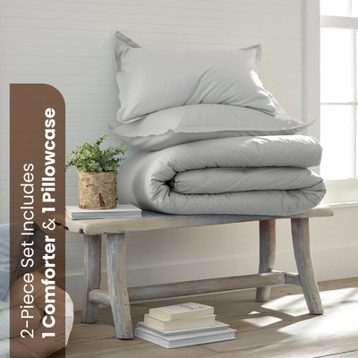 A bedding set displayed in a bright room. The set includes a folded light grey comforter and one white pillowcase.