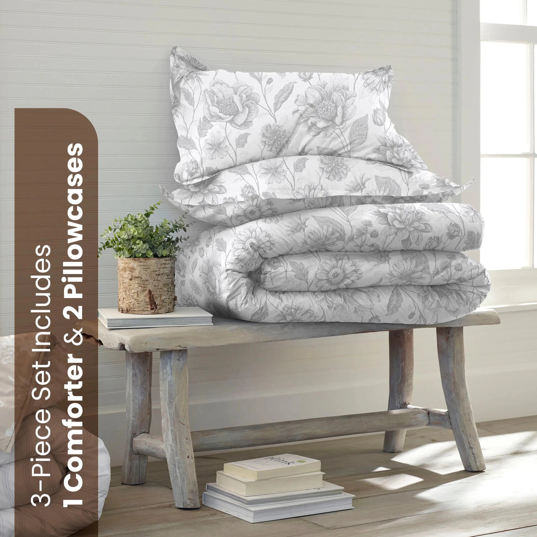 A bedding set displayed on a rustic wooden bench in a bright room. The set includes a white comforter and two matching pillowcase with a gray floral pattern.