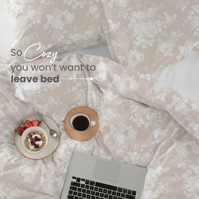 Floral-patterned comforter with a laptop, coffee, and plate of food on a light background.