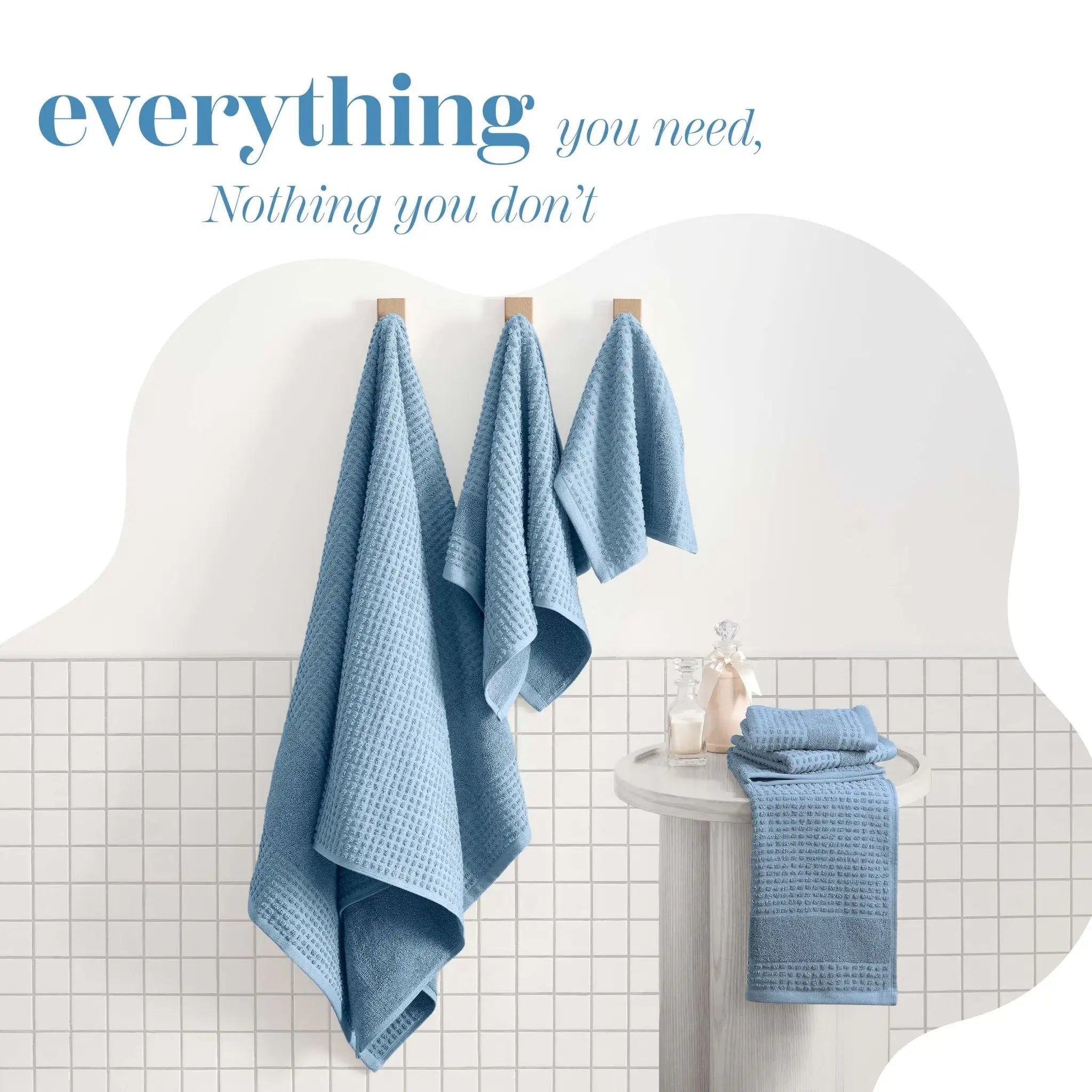 Three light blue towels hang on wooden pegs. The scene includes the text 'everything you need, Nothing you don't' at the top.