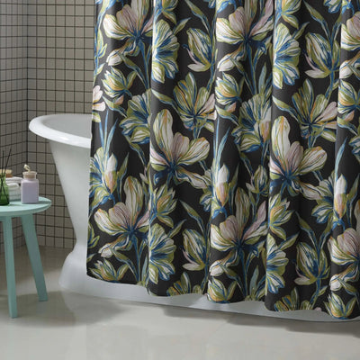 A floral shower curtain hanging in a bathroom, featuring large white and blue flowers with yellow-green centers on a dark charcoal background. A white clawfoot tub, a small mint green stool, and tiled walls are visible.